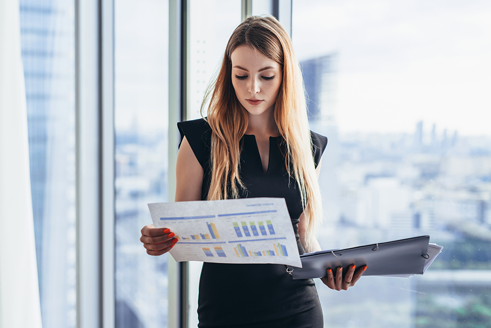 Female,Financial,Analyst,Holding,Papers,Studying,Documents,Standing,Against,Window